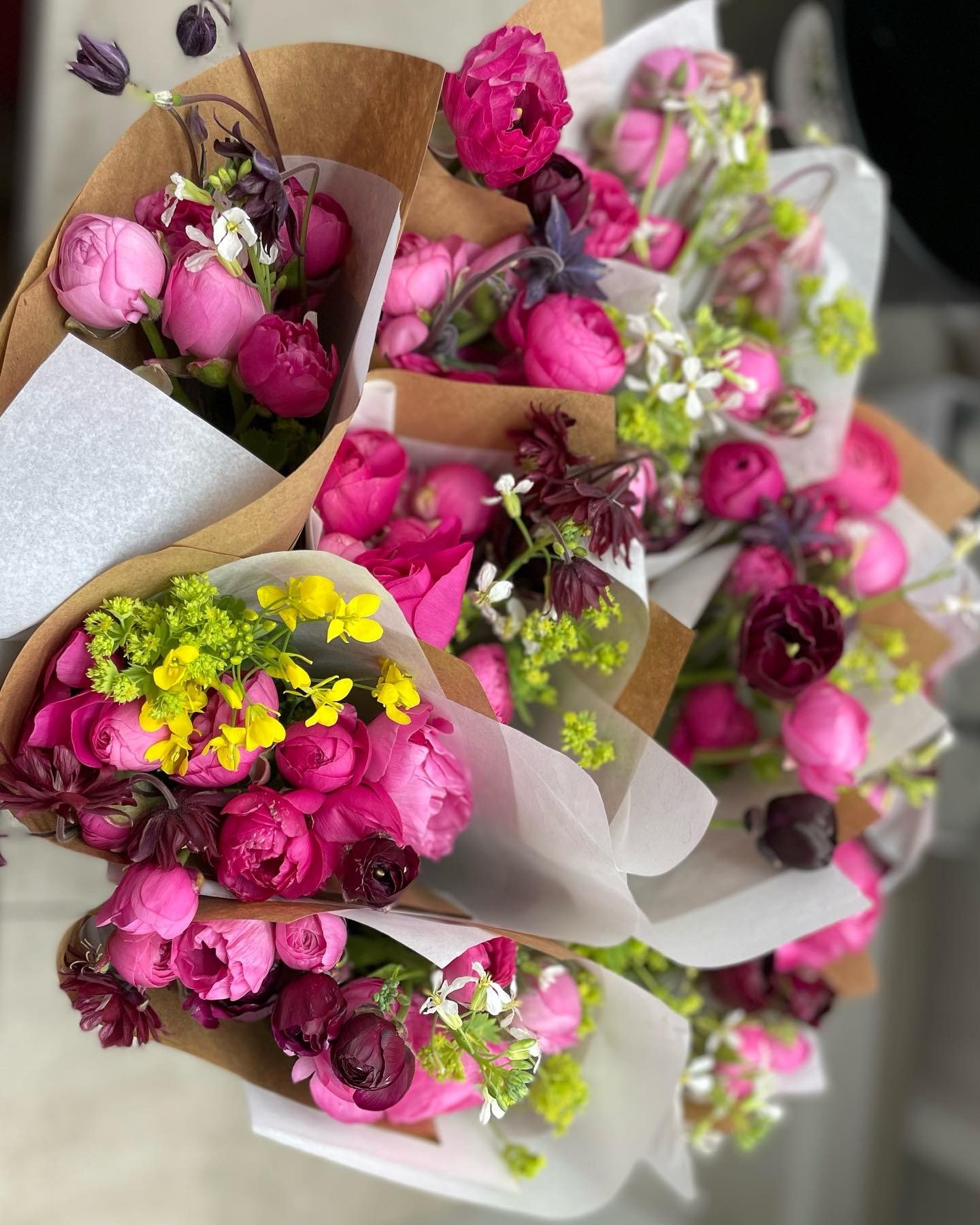 Colorful bouquets of pink and purple flowers, wrapped in brown paper, showcasing a variety of blooms including ranunculus and peonies, perfect for gifting or home decoration.